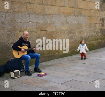 Funny little girl et l'homme qui joue de la guitare dans une rue proche de la cathédrale. Santiago de Compostela, Espagne, 22 février 2019. Banque D'Images