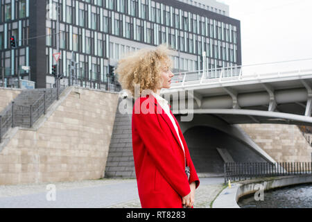 Allemagne, Berlin, jeune femme blonde portant des anglaises avec manteau rouge Banque D'Images