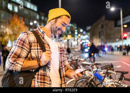 UK, Londres, l'homme la navette de nuit dans la ville et à la recherche à son téléphone Banque D'Images