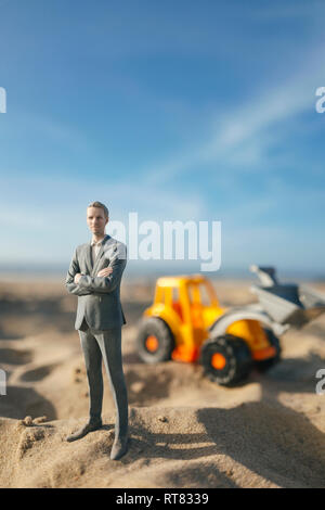 Figurine homme debout sur le sable avec toy digger, l'investissement dans l'accession à la propriété Banque D'Images