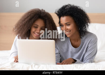 African mother lying on bed with teen fille internet navigation Banque D'Images