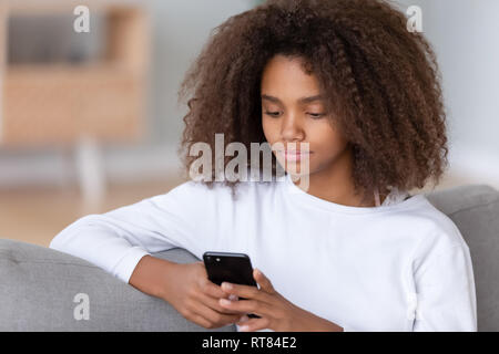 Close up african teenager girl sitting on sofa using smartphone Banque D'Images