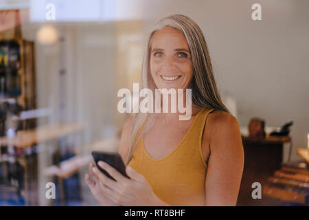 Portrait of smiling businesswoman with cell phone dans sa boutique Banque D'Images