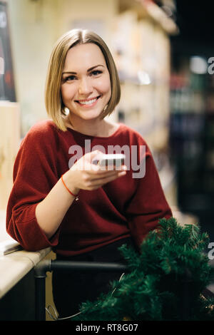 Image de blonde vendeur avec téléphone dans les mains, en tablier noir sur fond flou. Banque D'Images