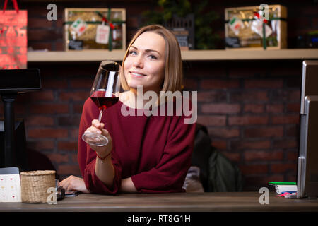 La photo d'une femme vendeur avec un verre de vin debout derrière la caisse enregistreuse Banque D'Images