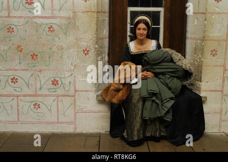 Une belle jeune femme en robe est Tudor authentique en appareil photo et sourit- elle est assise dans une vieille fenêtre et tient les vêtements.