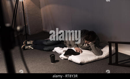 Homme étendu sur un matelas sur le plancher blanc in dark room Banque D'Images