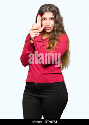 Young Beautiful woman wearing red sweater détenant des armes à feu symbolique avec geste de la main, à l'assassinat d'armes de tir visage en colère, Banque D'Images