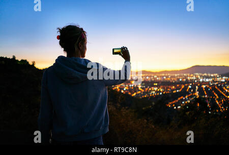 Le Chili, Santiago, woman taking cell phone photo dans les montagnes au-dessus de la ville au coucher du soleil Banque D'Images