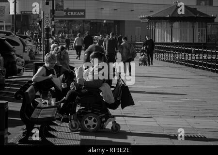 Les gens de l'image monochrome de manger un sac de chips sur New Brighton Merseyside promenade le long d'une journée au début du printemps. Banque D'Images