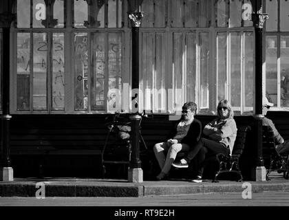 Image monochrome de 2 femmes assises sur un banc dans un abri victorien à New Brighton Merseyside UK. Banque D'Images