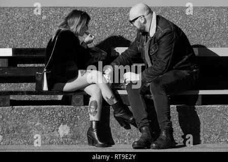 Image Monochrome d'une jeune femme aux jambes tatouées assis sur un banc de manger avec un ami. Banque D'Images