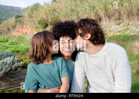 Famille heureuse assis sur un banc dans un jardin, père et fils s'embrasser mère Banque D'Images