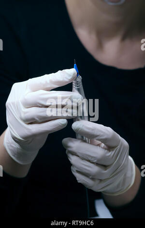 Coiffeur professionnel en noir avec des gants blancs en mettant l'aiguille de tatouage spécial pour la préparation de l'appareil maquillage permanent en studio de beauté, Close up Banque D'Images