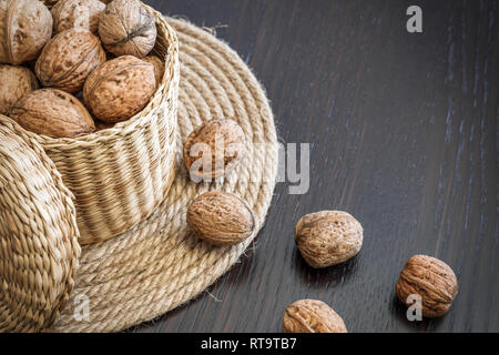 Ensemble de noix en panier et éparpillés sur une table en bois foncé, de l'espace pour le texte. Concept d'aliments sains. Banque D'Images