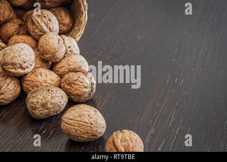 Ensemble de noix en panier et éparpillés sur une table en bois foncé, de l'espace pour le texte. Concept d'aliments sains. Banque D'Images