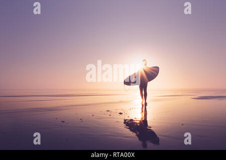 La silhouette d'un surfeur debout sur une plage au coucher du soleil. Avec sunflare. Saunton, Devon, UK. Banque D'Images