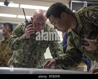 YOKOSUKA, Japon (fév. 7, 2019) maître d'armes de 1re classe Tommy Hayner, gauche, affectés à des activités de la flotte (FLEACT) Yokosuka, écoute des rapports sur les incidents en cours comme le Sgt. Konno Akira, droit, attribué à l'Autodéfense de masse Japon 2ème compagnie, 13e Régiment d'infanterie, indique le site sur un site au cours de l'effort de protection et de protéger en 2019, un accord bilatéral entre les États-Unis et les gouvernements japonais, à bord d'FLEACT Yokosuka. FLEACT fournit de Yokosuka, entretient et exploite des installations et des services de base à l'appui de la 7ème Flotte américaine déployée sur l'avenir des forces navales, 71 tenan Banque D'Images