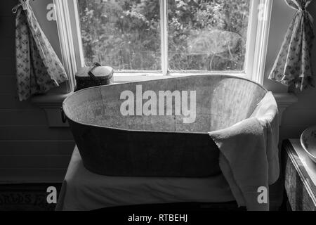 Une ancienne école metal baignoire dans la fenêtre d'une maison, avec une serviette drapée sur la fin de la baignoire, tourné en noir et blanc pour donner un vrai supplément vintage Banque D'Images