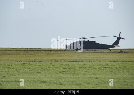 Un membre d'équipage au sol de l'armée américaine, affecté à la 1re Brigade d'aviation de combat, 1re Division d'infanterie, vous attend pour des instructions à côté d'un UH-60 Black Hawk, que d'autres aéronefs quittent la base aérienne de Chièvres, Belgique, 7 février 2019. La Base Aérienne de Chièvres a servi comme une zone d'étape intermédiaire avant la 1re Brigade d'aviation de combat se déploie à l'Allemagne, la Pologne, la Lettonie et la Roumanie pendant neuf mois pour former avec les partenaires de l'OTAN à l'appui de la résolution de l'Atlantique. Banque D'Images