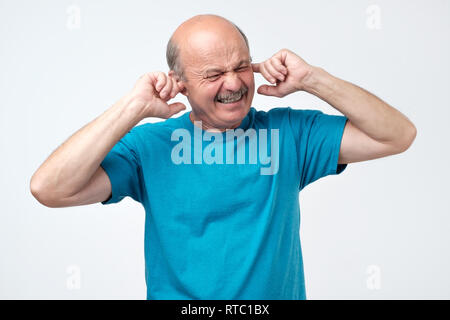 Senior hispanic chauve boucher les oreilles avec les doigts audience des sons forts de la musique d'appartement au-dessus Banque D'Images