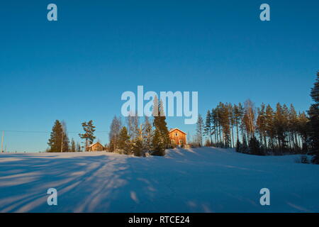 Une maison de ferme est éclairé par le faible soleil d'hiver. Le casting est près de la forêt de longues ombres sur la neige. Banque D'Images