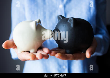 Deux tirelires en céramique- un blanc, une noire tenue par personne dans une chemise bleue avec des paumes ouvertes Banque D'Images