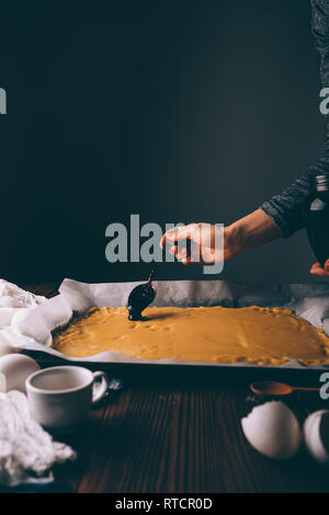 Jeune femme pâtisserie cuisson sur table de cuisine. La main de femme répandre de confiture sur feuilles laminées de pâte à cuire des tartes. Banque D'Images