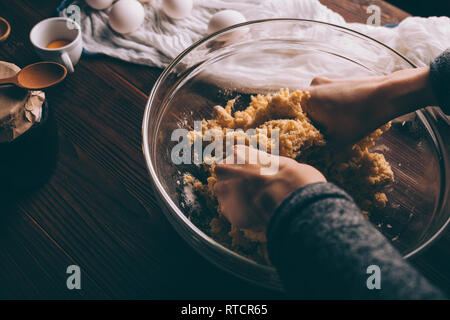 Vue de dessus de la pâte dans le bol de pétrissage les mains sur la table de cuisine à côté des oeufs, jaune et le pot de confiture, close-up. Banque D'Images