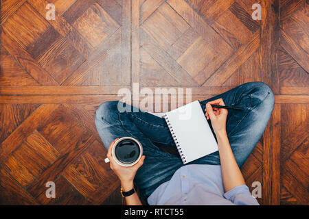 Concept de travail confortable à la maison. Vue supérieure de la femme assis sur un plancher en bois écrit dans l'ordinateur portable et de boire du café. Banque D'Images