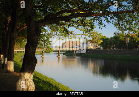 Vue sur le pont principal de l'autre côté de la rivière Uzh dans Uzhhorod dans coucher du soleil chaud de la lumière. Des arbres verts poussant à proximité, leurs branches suspendues sur la rivière Banque D'Images