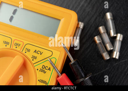 Vérifier les fusibles en verre à l'aide de l'appareil. Travaux électriques simples dans un atelier d'accueil. Fond sombre. Banque D'Images