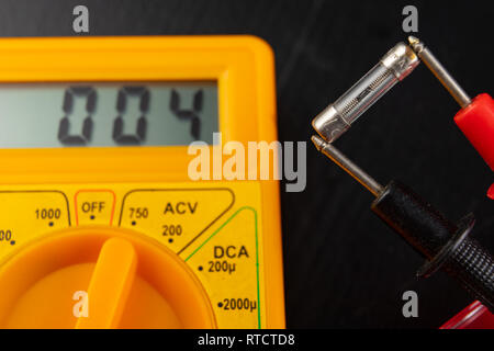 Vérifier les fusibles en verre à l'aide de l'appareil. Travaux électriques simples dans un atelier d'accueil. Fond sombre. Banque D'Images