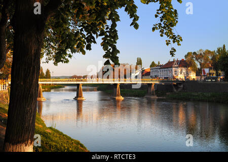 Vue sur le pont principal de l'autre côté de la rivière Uzh dans Uzhhorod dans coucher du soleil chaud de la lumière. L'arbre vert haut poussant à proximité, ses branches suspendues sur la rivière Banque D'Images