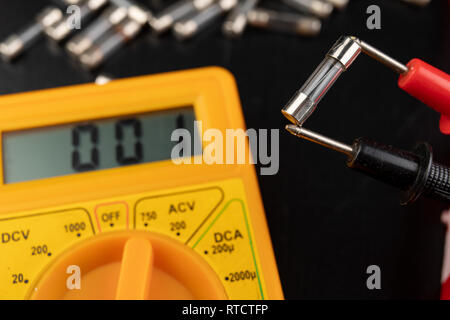 Vérifier les fusibles en verre à l'aide de l'appareil. Travaux électriques simples dans un atelier d'accueil. Fond sombre. Banque D'Images