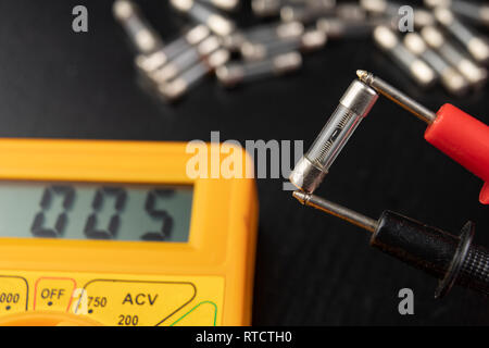 Vérifier les fusibles en verre à l'aide de l'appareil. Travaux électriques simples dans un atelier d'accueil. Fond sombre. Banque D'Images