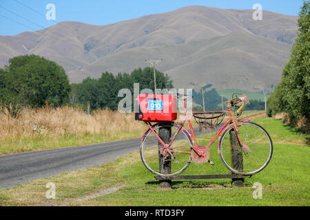 Une boîte aux lettres boîte aux lettres rouge attaché à une course vélo de route sur une route de campagne en milieu rural de l'île du sud de Nouvelle-Zélande Banque D'Images