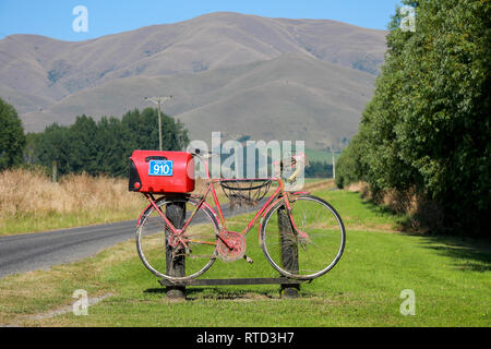 Une boîte aux lettres boîte aux lettres rouge attaché à une course vélo de route sur une route de campagne en milieu rural de l'île du sud de Nouvelle-Zélande Banque D'Images