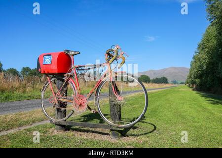 Une boîte aux lettres boîte aux lettres rouge attaché à une course vélo de route sur une route de campagne en milieu rural de l'île du sud de Nouvelle-Zélande Banque D'Images