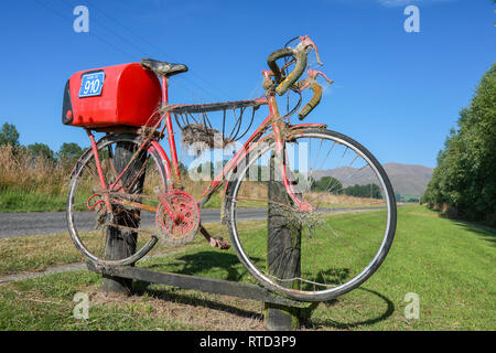 Une boîte aux lettres boîte aux lettres rouge attaché à une course vélo de route sur une route de campagne en milieu rural de l'île du sud de Nouvelle-Zélande Banque D'Images