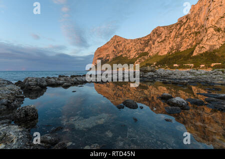 Beaux nuages épars au coucher du soleil à Barcarello, avec le promontoire de Capo Gallo reflétée sur l'eau calme. Palerme, Sicile. Banque D'Images