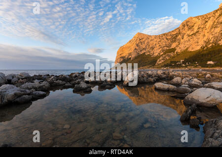 Beaux nuages épars au coucher du soleil à Barcarello, avec le promontoire de Capo Gallo reflétée sur l'eau calme. Palerme, Sicile. Banque D'Images