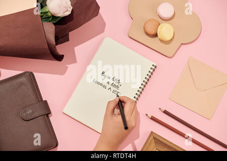 La main de femme à la plume écrit sur la carte de vœux sur la table. Roses roses. Des fleurs fraîches. Banque D'Images