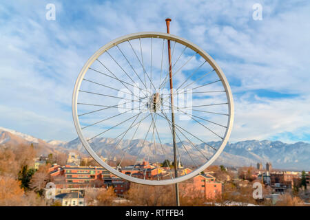 Jante de roue de vélo de montagne et de maisons contre ciel. Location jante accrochée à un pôle rouillée avec des maisons et bâtiments en arrière-plan. Une neige lointaine Banque D'Images