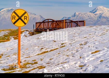 Signe de fer contre un pont et la montagne enneigée. Railroad Crossing sign sur une pente couverte de neige dans la région de Eagle Mountain, Utah. Un pont et le majestueux Mo Banque D'Images