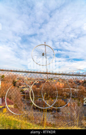 Clôture à mailles de chaîne rouillée avec des jantes de vélo. Vieux vélo jantes suspendu par une clôture à mailles de chaîne rouillée. Maisons et montagne sous ciel bleu rempli w Banque D'Images