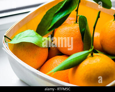 Quelques oranges avec des feuilles dans un panier, Orange mandarine dans un panier sur un fond blanc. Banque D'Images