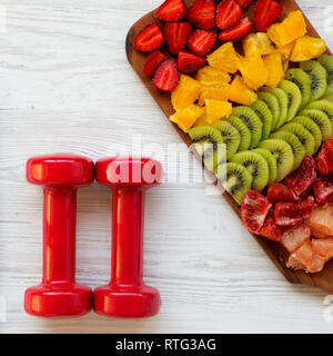 Concept de remise en forme, plan de régime. Les haltères et les fruits hachés sur la surface en bois blanc, vue du dessus. Mise à plat. Banque D'Images