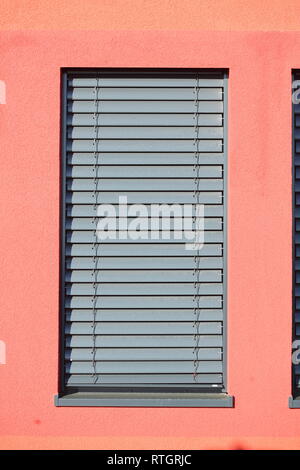 Fenêtre avec stores volets sombre sur un mur de la maison rouge Banque D'Images