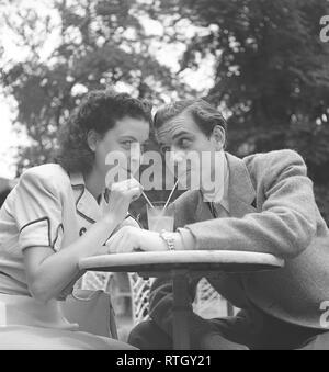 1940 Style de vie. Un jeune couple dans un café en plein air. Ils boivent dans le même verre de limonade avec paille. La Suède. Kristoffersson Photo Ref U89-2. Suède 1946 Banque D'Images